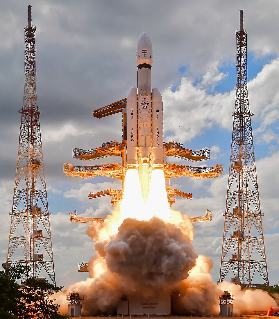 The LVM3-M4 rocket lifting off from the Second Launch Pad at Sriharikota in a plume of flame and smoke, lightning towers standing on either side