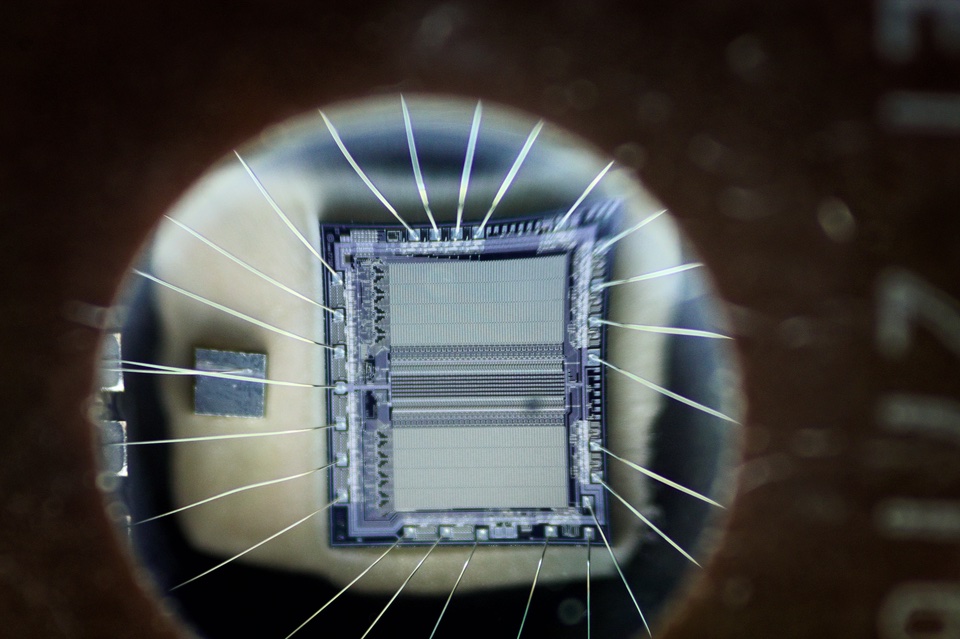 Macro photograph looking through the round quartz window of an EPROM chip at the silicon die and its fan of gold bond wires inside the package