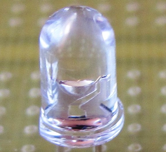 Close-up of a clear 5 mm through-hole light-emitting diode, the reflector cup, semiconductor chip and bond wire visible inside its epoxy dome