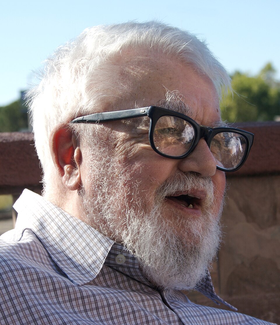 Close head-and-shoulders portrait of John McCarthy outdoors, with white hair and beard and thick black-framed glasses