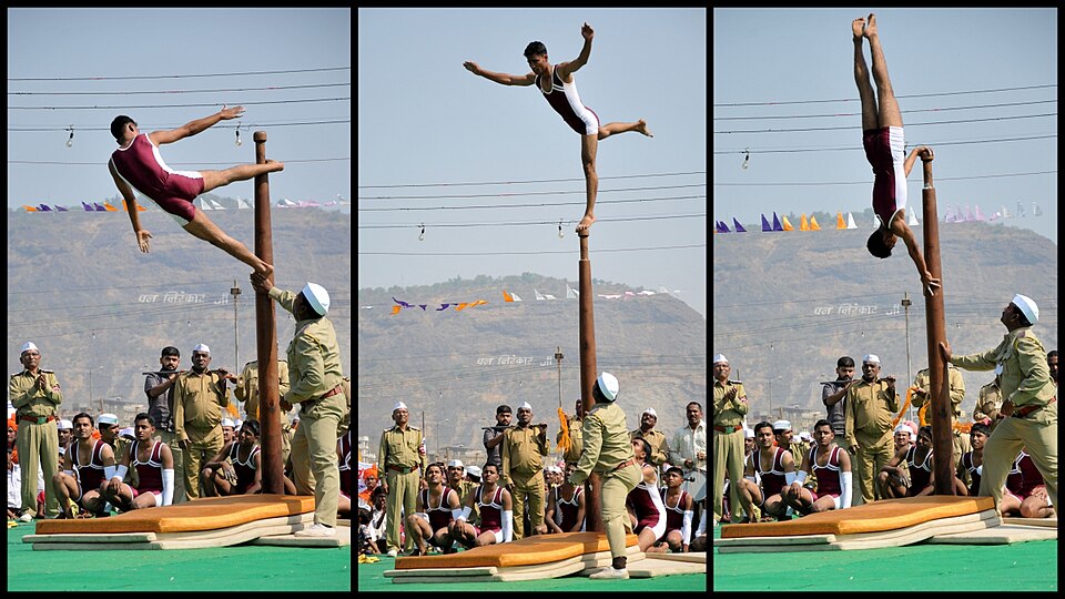 Three frames of a mallakhamb display: athletes holding balances and an inverted hold on a vertical wooden pole set on a mat, watched by a seated crowd