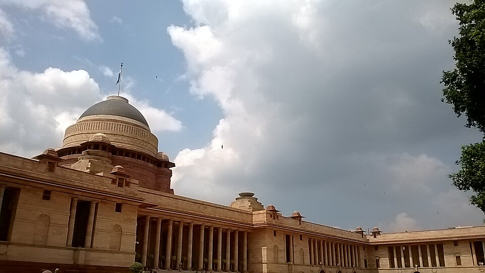 Rashtrapati Bhavan seen from its forecourt, the great copper dome rising above a long sandstone colonnade under a cloudy sky