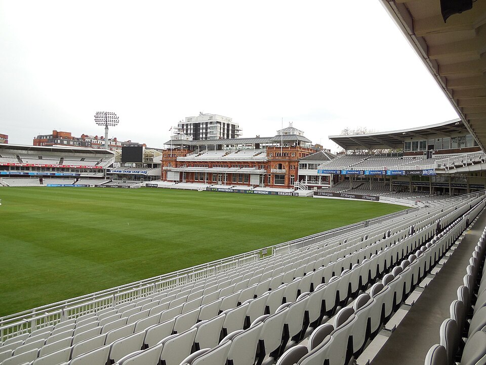 The red-brick Victorian Pavilion at Lord's Cricket Ground seen across the empty outfield from tiers of grey seats