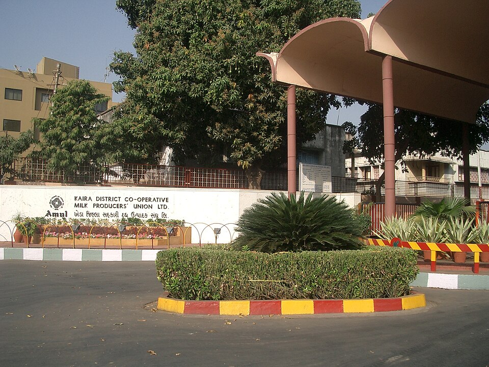 The entrance drive of the Amul dairy at Anand, with a boundary wall lettered Kaira District Co-operative Milk Producers' Union Ltd behind flower beds