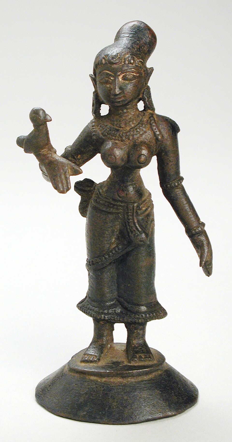 A South Indian bronze figure of the poet-saint Andal standing on a round pedestal, a parrot perched on her raised left hand
