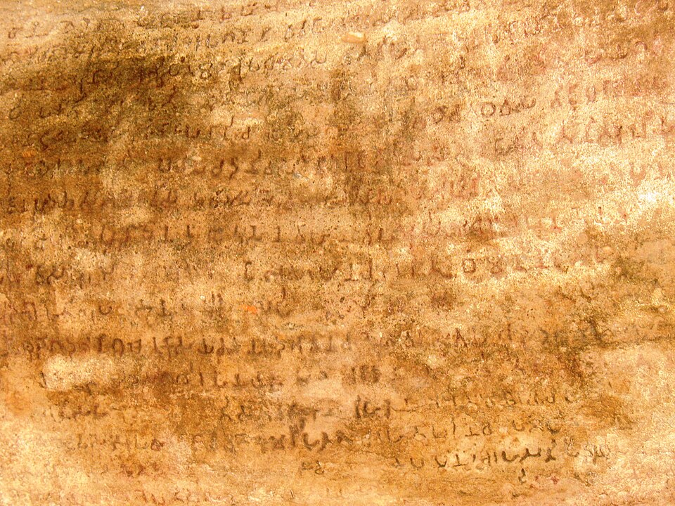 Close view of the Hathigumpha inscription: many lines of Brahmi characters incised across a weathered honey-coloured rock surface