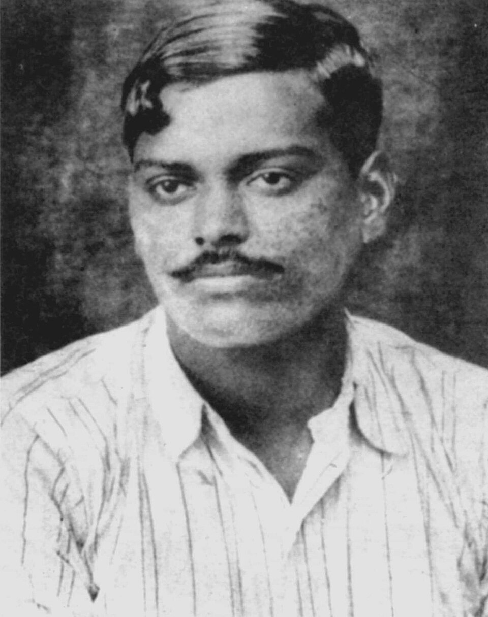 Historic black-and-white portrait photograph of the young Chandrashekhar Azad with a thick moustache and centre-parted hair, wearing an open-collared striped shirt
