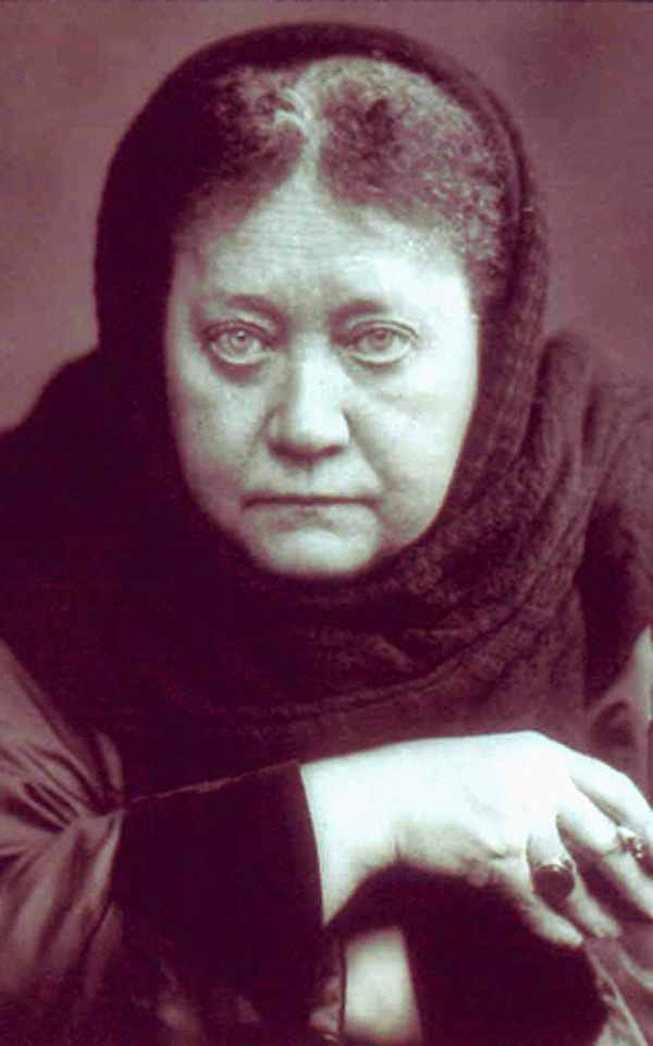 Sepia portrait photograph of Helena Petrovna Blavatsky, an older woman in a dark hooded wrap with her hands clasped in front of her, a ring on one finger