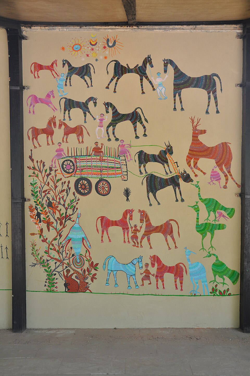A Bhil Pithora wall painting: rows of brightly dotted horses, bulls, deer, peacocks, a bullock cart and a flowering tree filling a wall panel