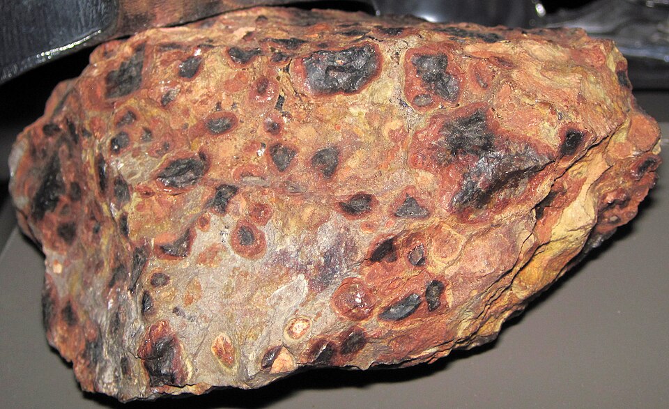 A reddish-brown pisolitic bauxite specimen, its surface studded with rounded pea-like concretions in rust and dark tones