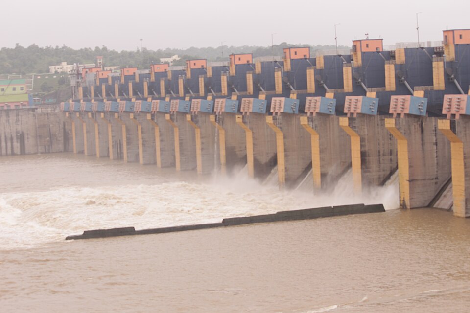 The Omkareshwar Dam on the Narmada in spate, water jetting from beneath its long row of gated spillway piers into the brown river below