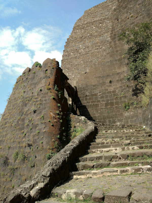 Weathered stone ramparts of Asirgarh Fort rising steeply above a flight of worn stone steps that climb towards an arched gateway