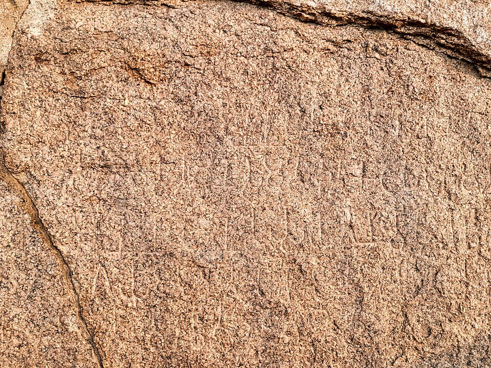 Rows of weathered Brahmi characters incised into a reddish granite rock face - the Gujarra Minor Rock Edict of Ashoka