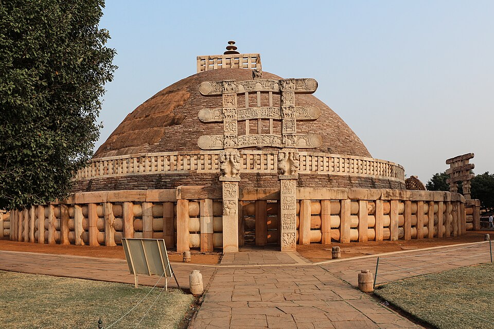 The Great Stupa at Sanchi: a large hemispherical brick dome ringed by a stone railing, with a richly carved torana gateway at its entrance