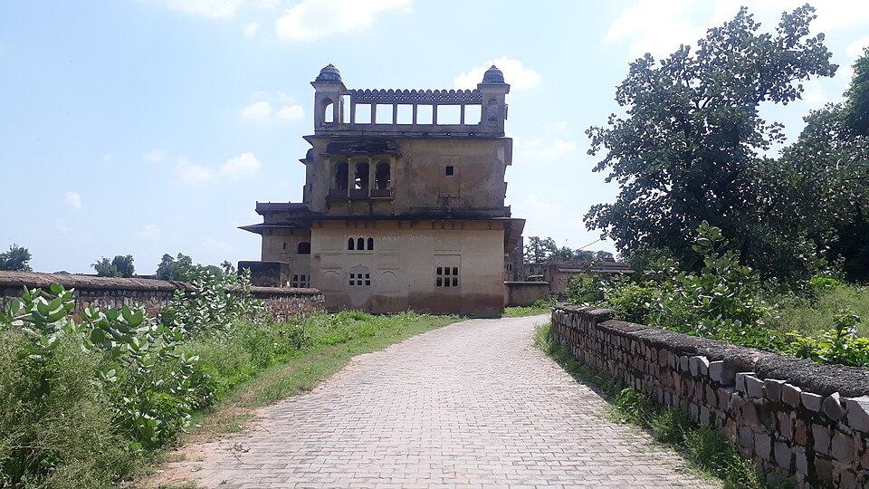 The Rai Praveen Mahal at Orchha, a weathered two-storey sandstone palace with an open pillared pavilion on its roof, reached by a paved path
