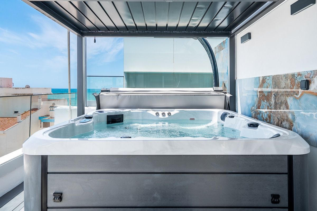 Penthouse 2 rooftop hot tub under a louvred pergola, with a glass balustrade and the Atlantic in the distance