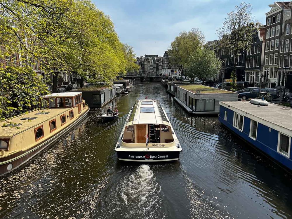 Tourists in a boat on the canals of Amsterdam. Skipper wearing an orange jacket.