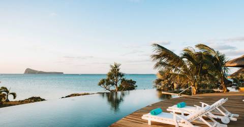 Pool och solstolar i solnedgång vid hav i Paradise Cove, Mauritius