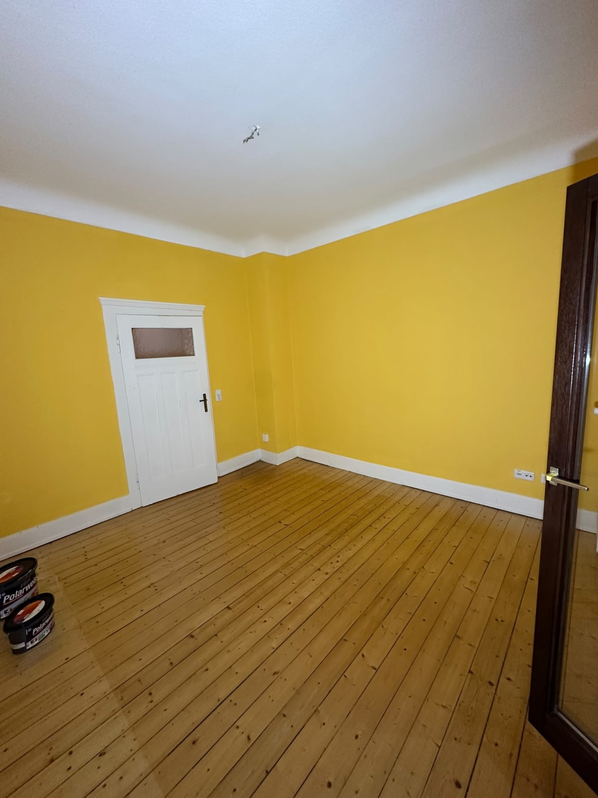 Frisch gestrichenes Zimmer mit gelben Wänden, weißer Decke und Holzdielen – Malerarbeiten in einer 3-Zimmer-Wohnung in Wiesbaden