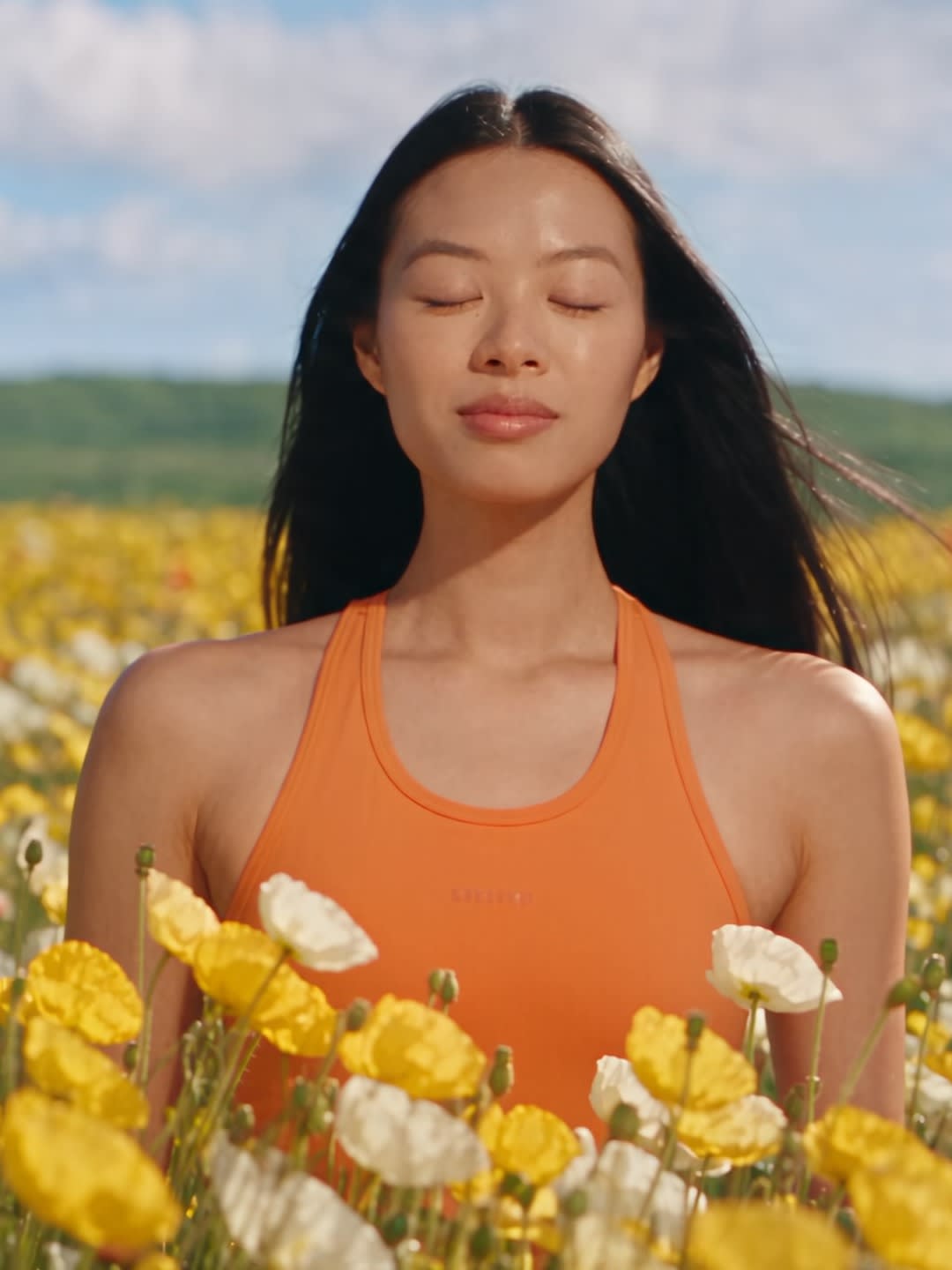 Alexandra Lim, with eyes closed in a field of yellow and white poppies under a blue sky