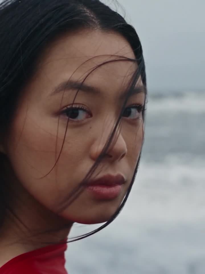 Alexandra Lim, in red silk on a black sand beach in Iceland, from above, then looking to camera