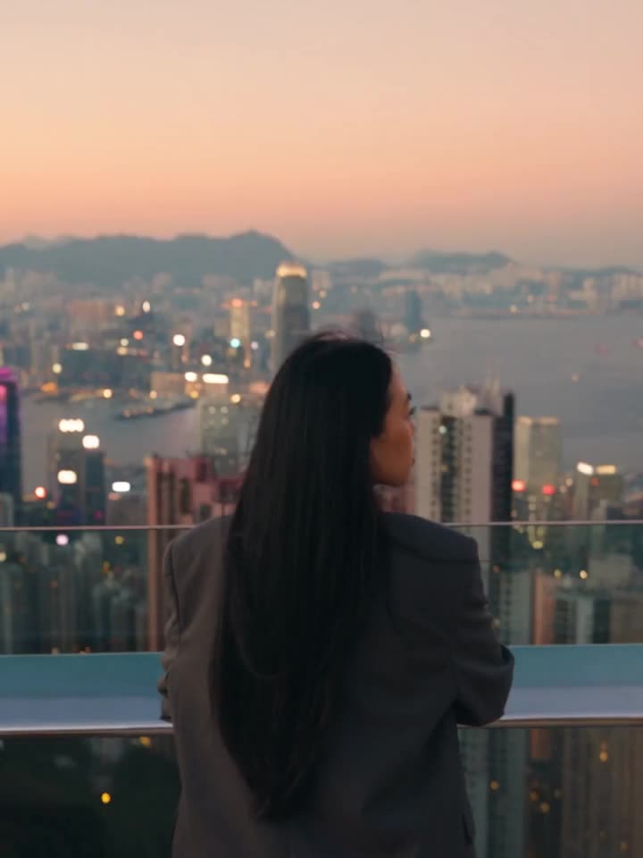 Alexandra de espaldas en una azotea de Hong Kong al atardecer, mientras la cámara sube y revela la bahía