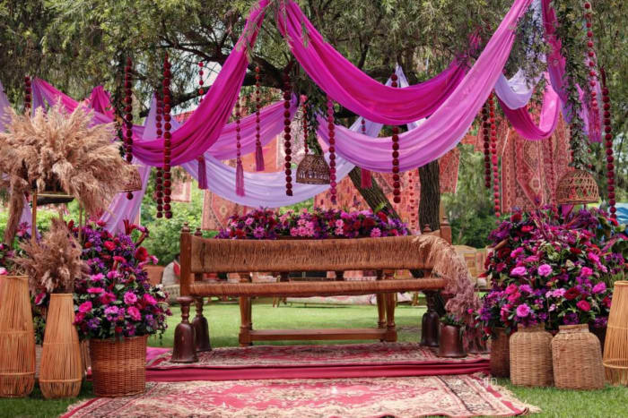 Vibrant pink bohemian mehendi setup with flowing drapes and pampas grass