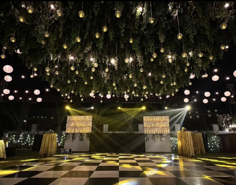 Outdoor wedding sangeet dance floor with checkered tiles and greenery ceiling with hanging globe lights — Panigrahana sangeet decor