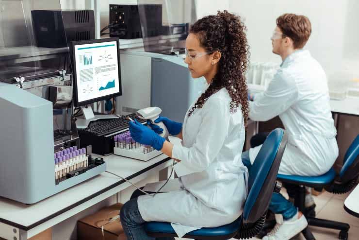 Woman in lab coat handles specimen in front of computer screen