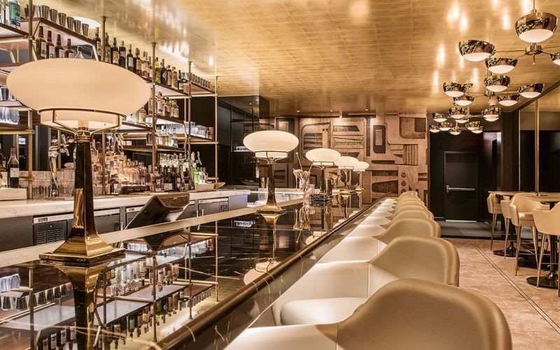 Bar with luxurious art deco decorations, lamps, chandeliers and an alcohol rack illuminated by lights.