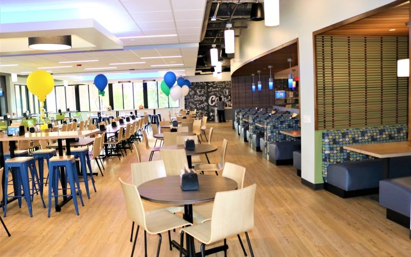 The dining room at Aurora University with benches, chairs, tables, some decorative balloons and pendant lights.