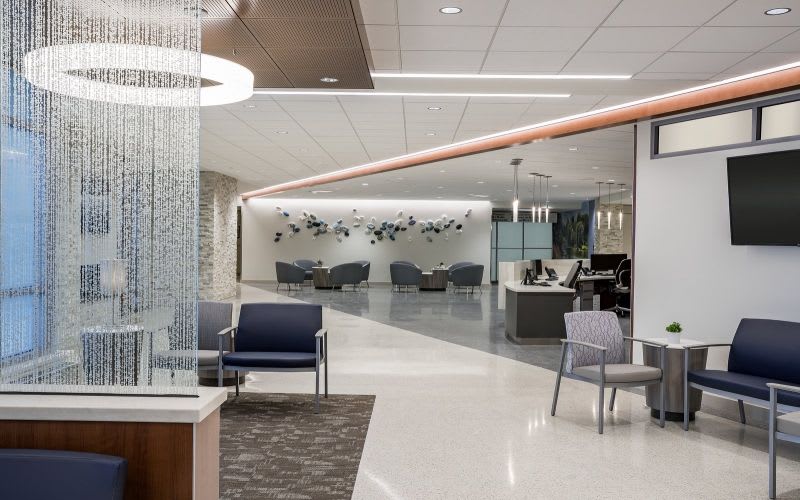 Lobby of the hospital with a front desk and modern pendant light fixtures, some tables and chairs.