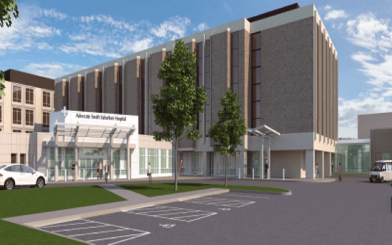 Entrance of the hospital next to a parking lot and some greenery.