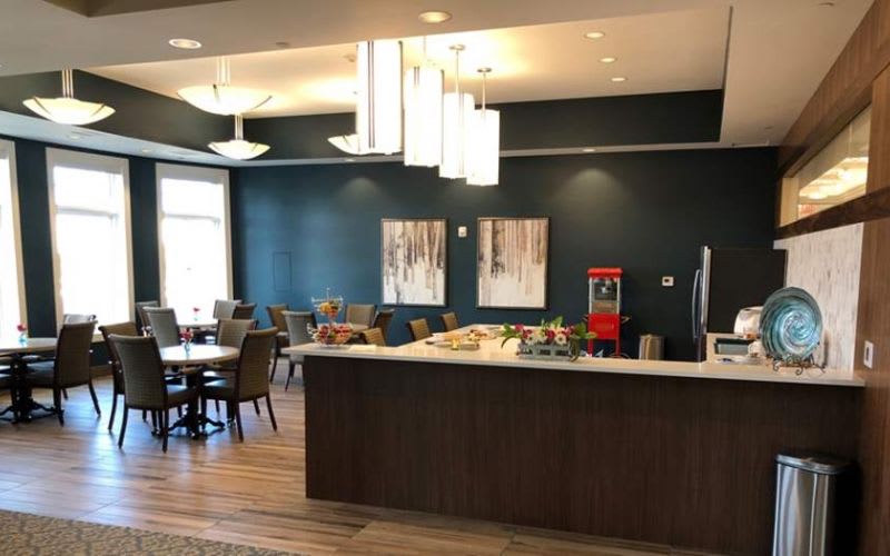 Dining room at Silverado Assisted Living with a couple tables, comfortable chairs, a fridge and large countertop space.