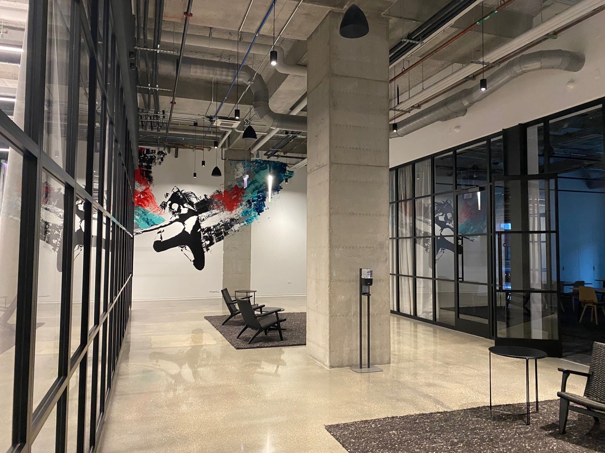 A hallway with large windows, art on the walls and seating options.