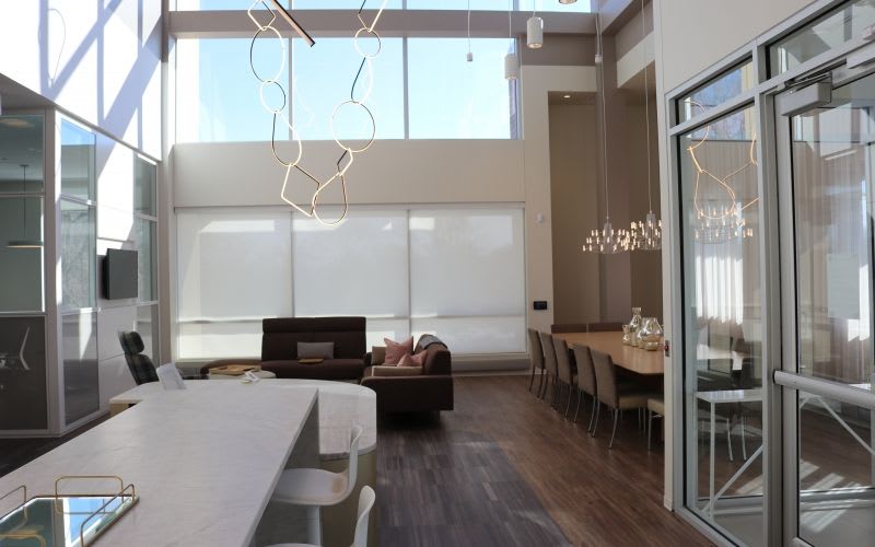 View of a long countertop and table, as well as a couple couches and few modern and decorated light pendant fixtures.