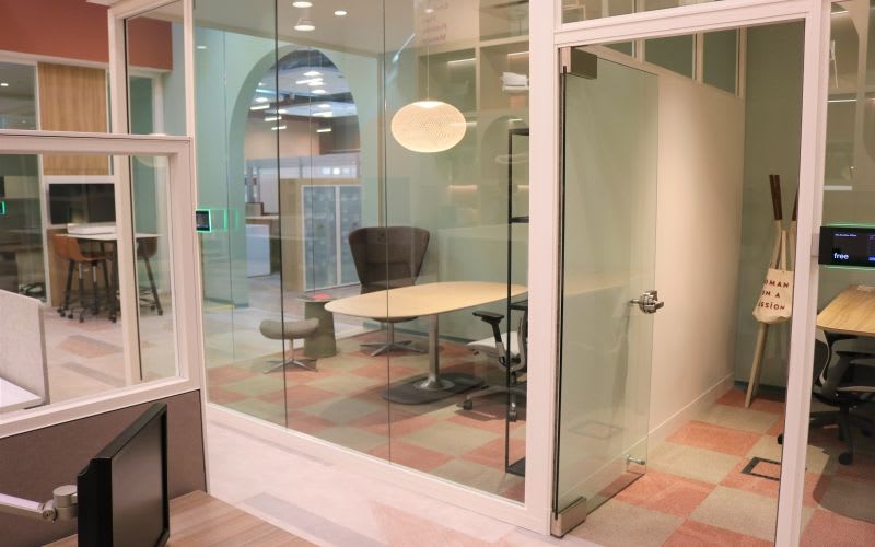Meeting rooms with glass walls, tables, chairs and light pendant fixtures inside.