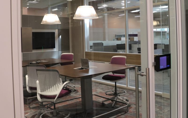 A meeting room with tall tables, chairs, glass walls and pendant lights.