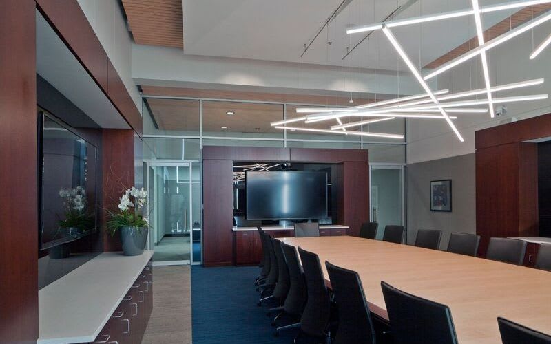 Meeting room with a long wooden table, chairs, a large screen and a modern pendant light fixture.