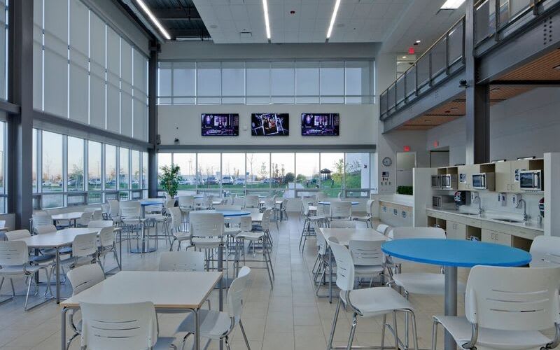 Atrium dining hall with various tables, chairs and a couple microwaves, sinks and televisions.