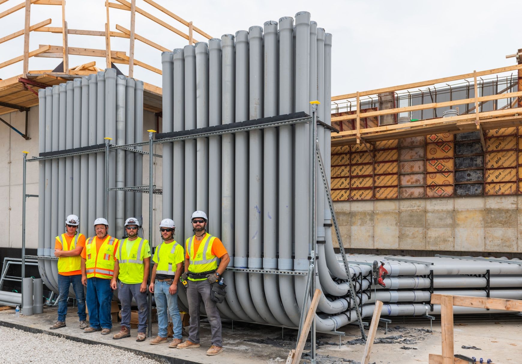 Connelly Electric on-site team smiling in front of conduits wearing construction vests and helmets.