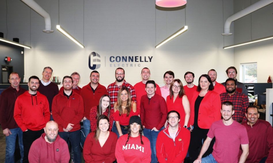 A group of employees at Connelly wearing red shirts in front of a Connelly logo.