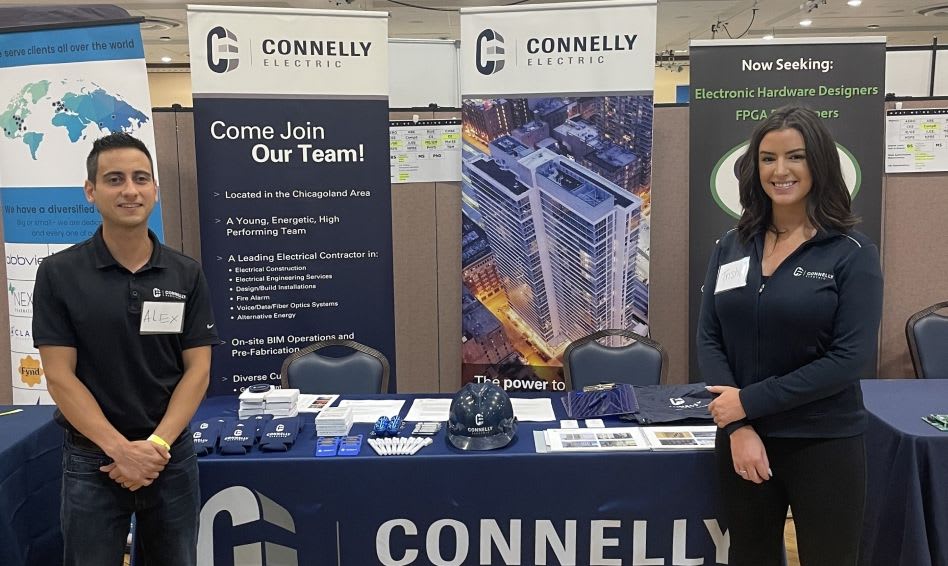 Two people smiling in front of a Connelly booth at a career fair.