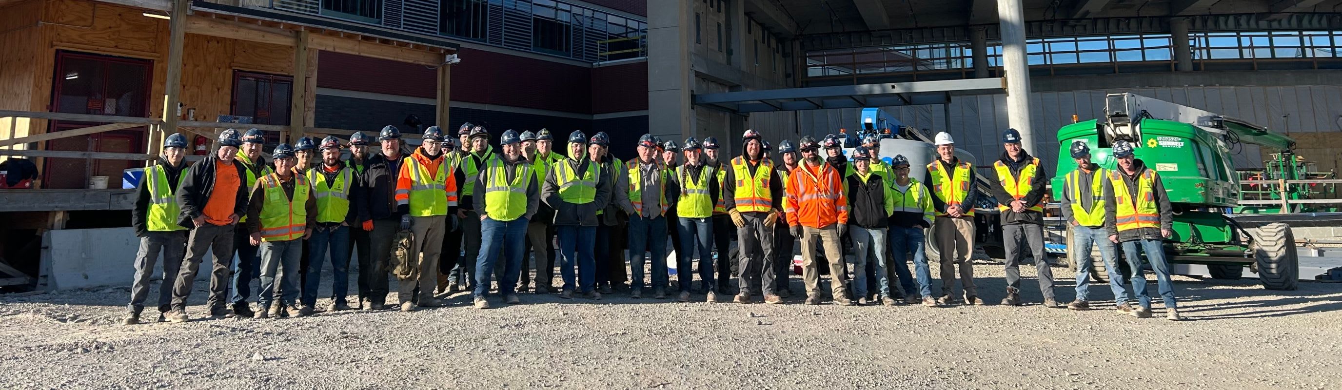 Connelly Electric on-site team smiling in front of conduits wearing construction vests and helmets.