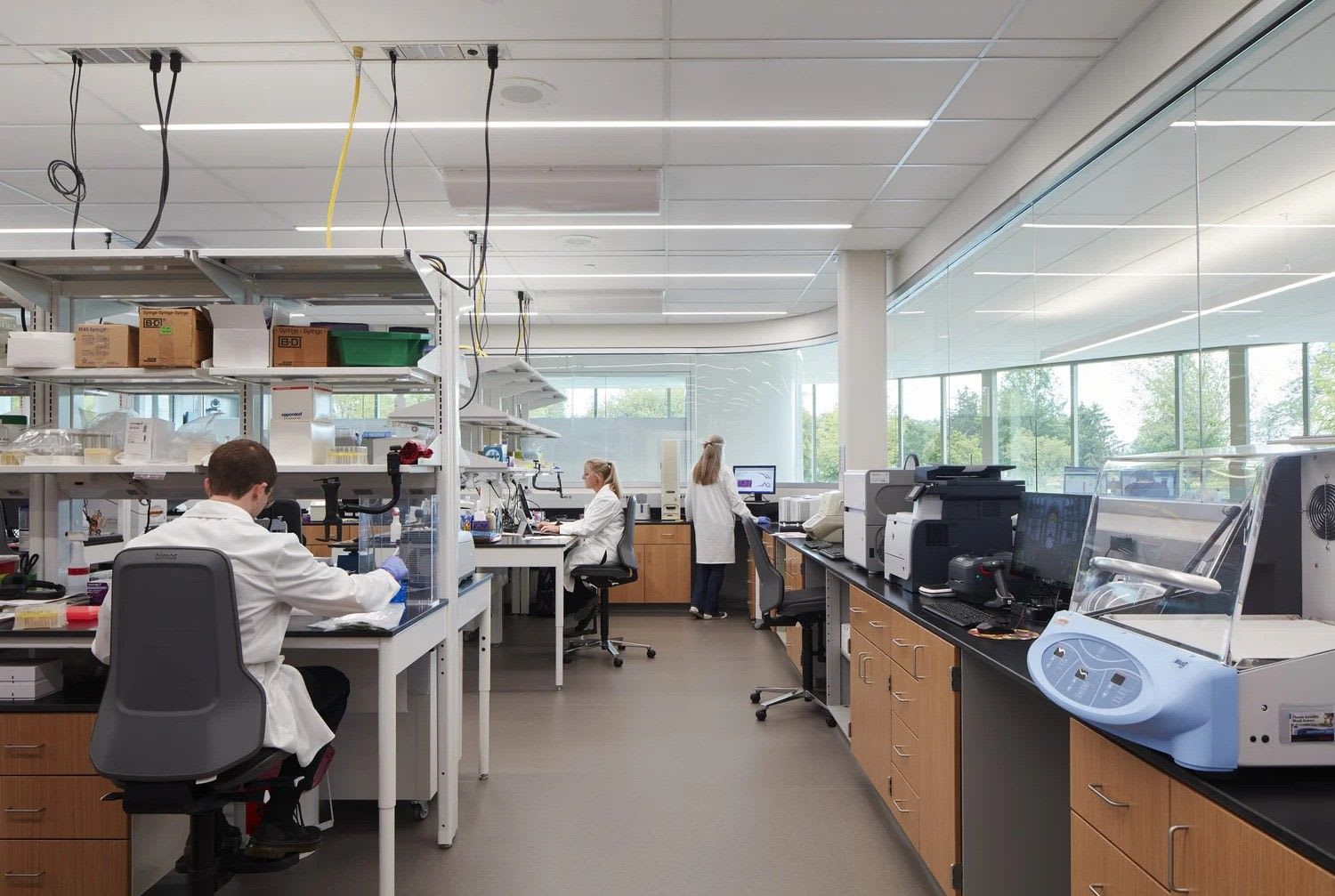 The inside of a laboratory, showing three researchers working alongside various machines, screens and boxes.
