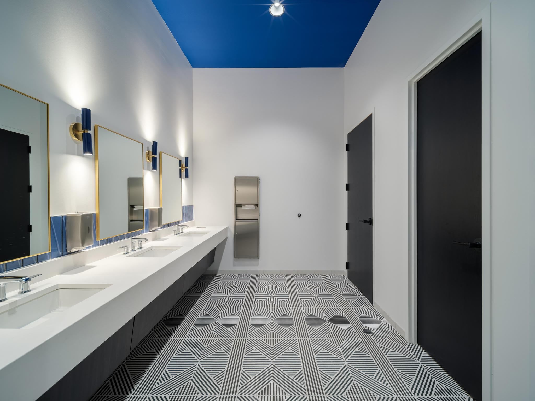 Bathroom featuring tile floor, gold-accent mirrors and modern light fixtures.