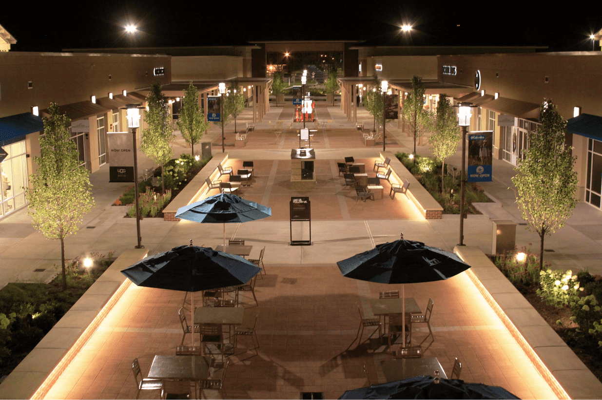 Outdoor outlets area with decorative lighting, scones and poles illuminated at night.