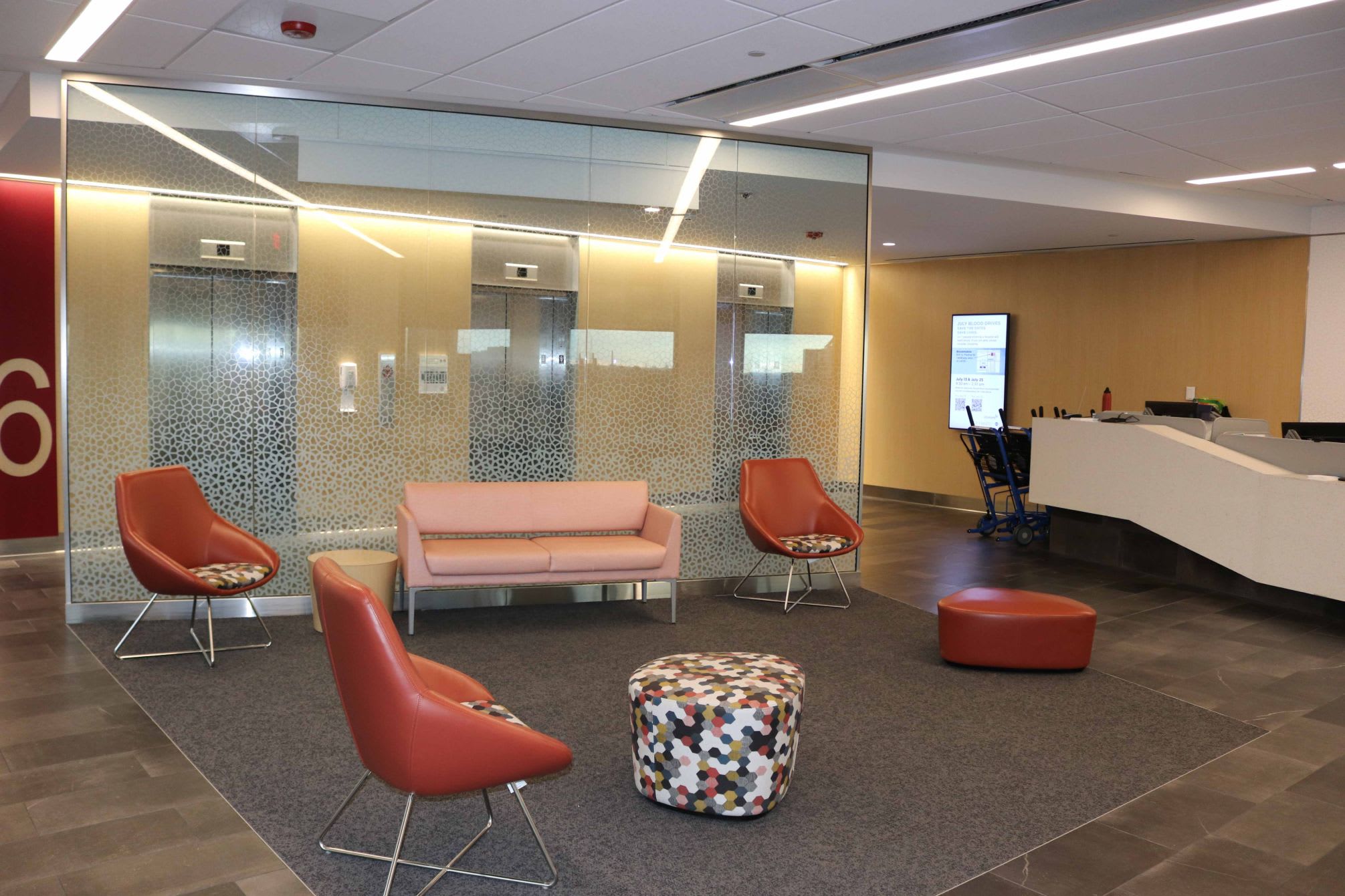 Room inside a medical building that is in front of an elevator and has a few chairs and a couch.