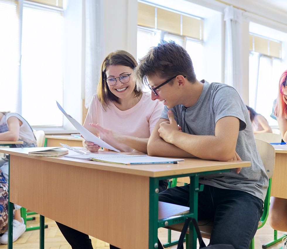 a teacher looking over a students work in the classroom