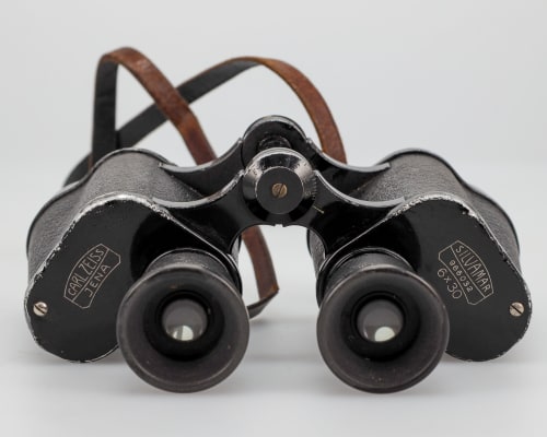 Black metal Zeiss 6x30 binoculars with a leather strap.